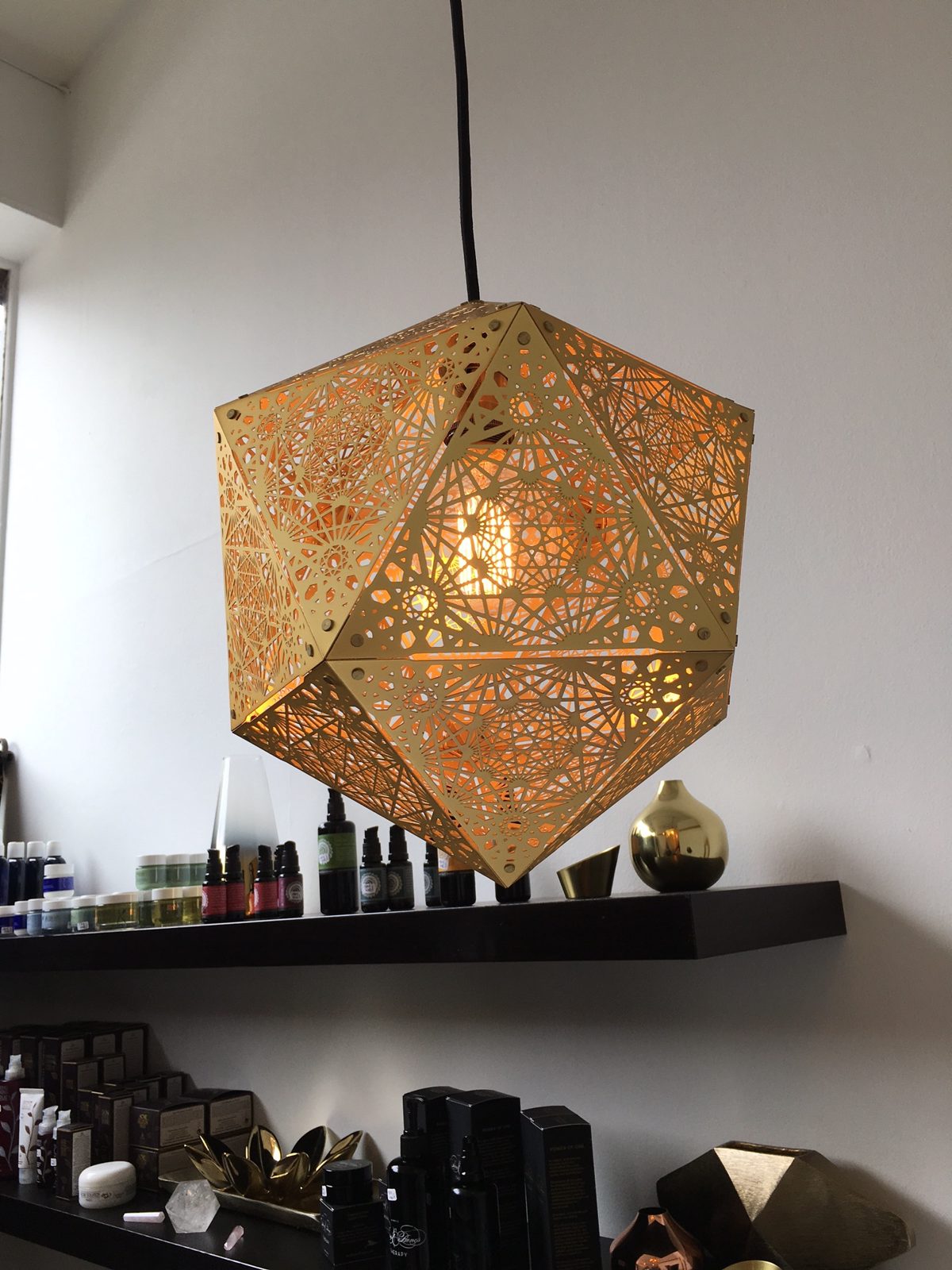 A gold faceted pendant lamp glowing over the retail shelves at Studio Soothe